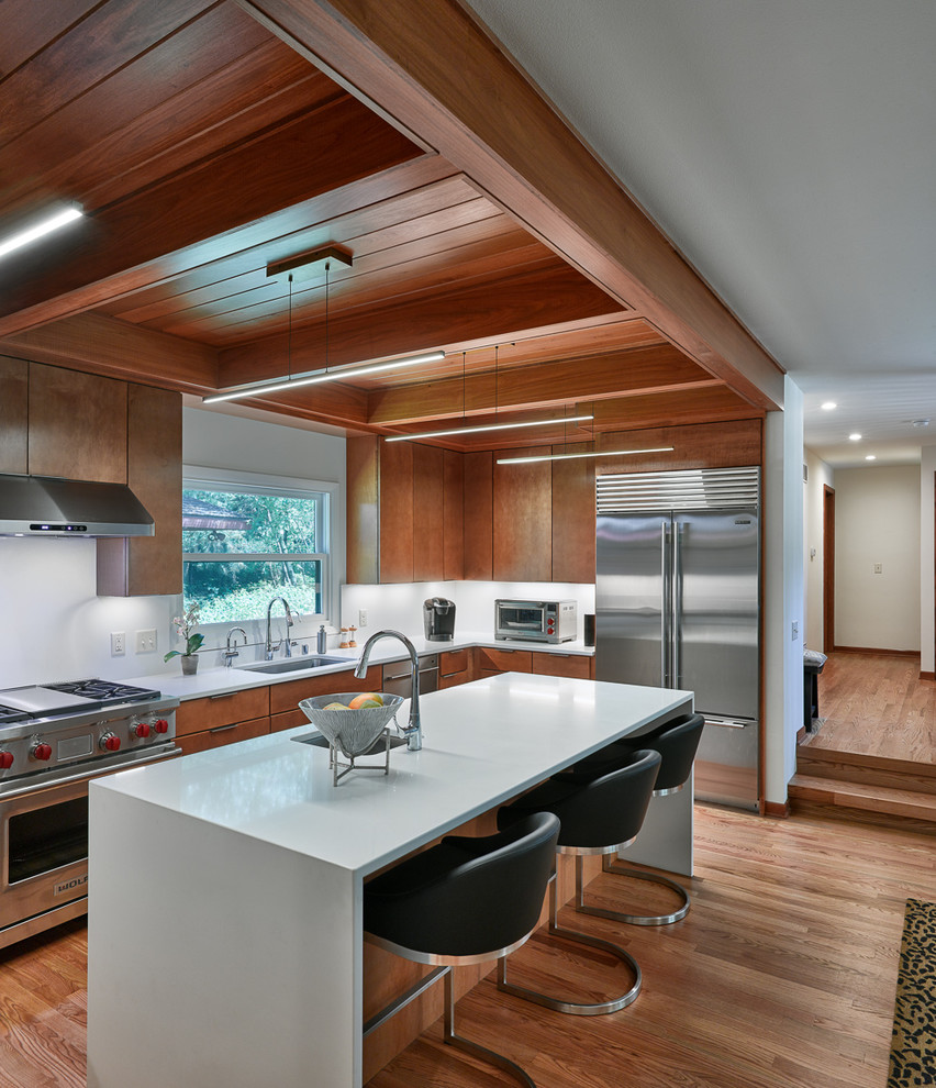 Design ideas for a midcentury l-shaped kitchen in Other with an undermount sink, flat-panel cabinets, medium wood cabinets, white splashback, stainless steel appliances, medium hardwood floors, with island, brown floor and white benchtop.