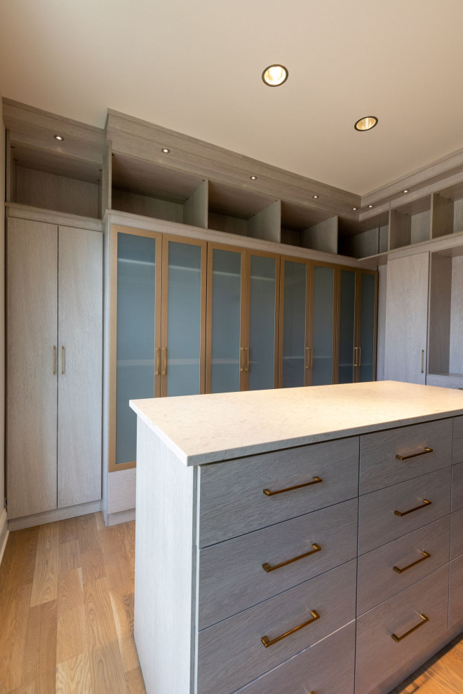 Inspiration for a large modern gender-neutral light wood floor walk-in closet remodel in Kansas City with glass-front cabinets and light wood cabinets