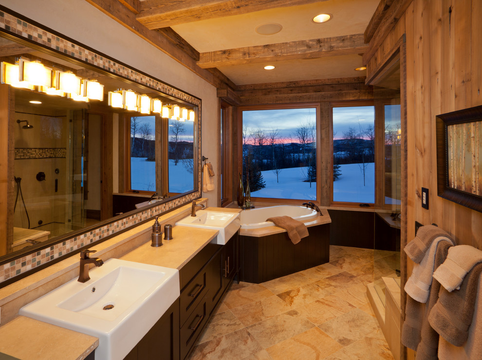 Inspiration for a large country master bathroom in Denver with shaker cabinets, dark wood cabinets, a corner tub, beige tile, beige walls and a trough sink.