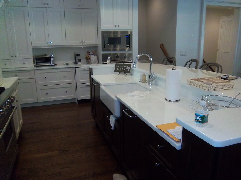 Inspiration for a large transitional l-shaped dark wood floor and brown floor eat-in kitchen remodel with a farmhouse sink, shaker cabinets, white cabinets, solid surface countertops, white backsplash, stainless steel appliances and an island