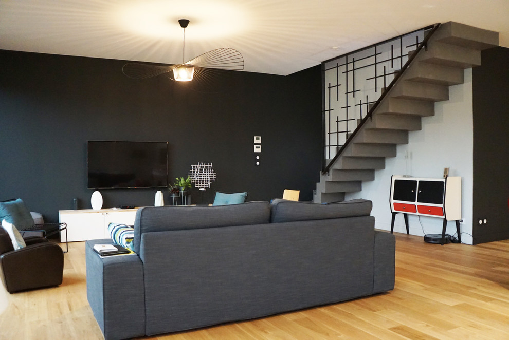 Inspiration for a mid-sized contemporary enclosed living room in Bordeaux with black walls, light hardwood floors, a wall-mounted tv and brown floor.