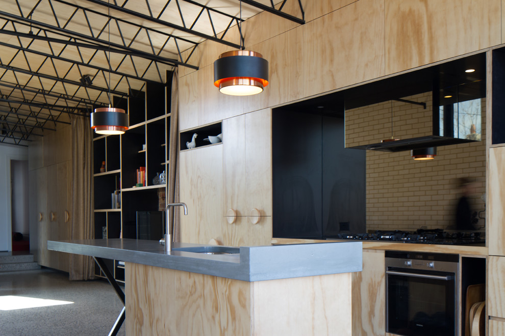 This is an example of an industrial single-wall open plan kitchen in Melbourne with an undermount sink, flat-panel cabinets, light wood cabinets, stainless steel appliances, with island, concrete benchtops, mirror splashback and concrete floors.