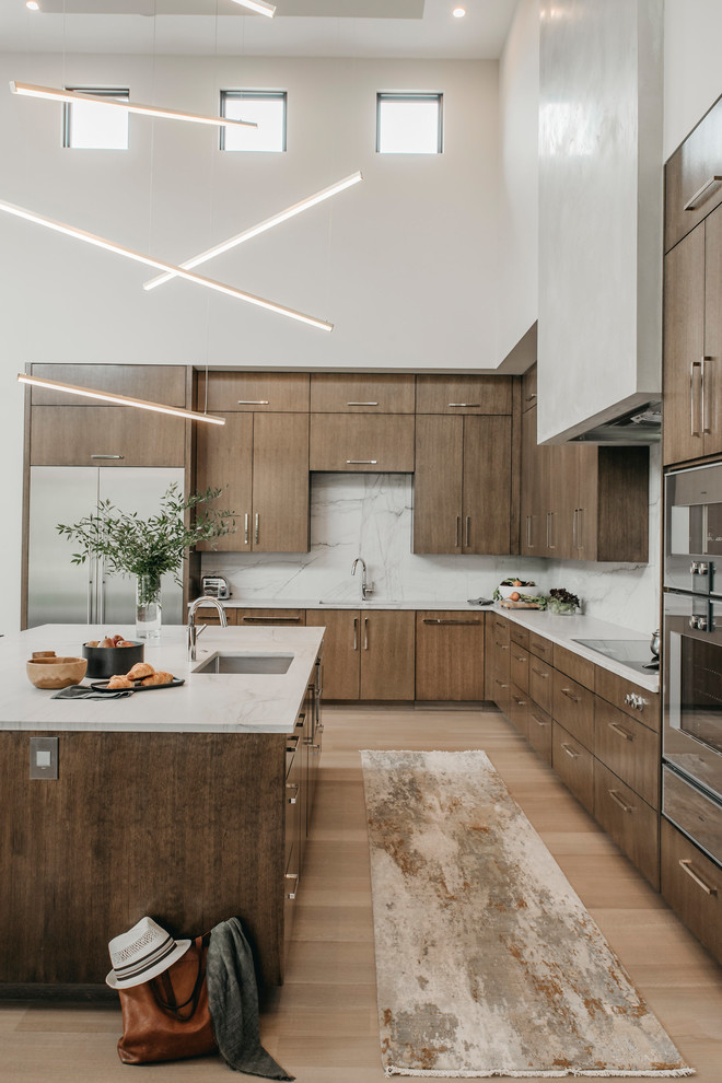 Inspiration for an expansive contemporary l-shaped eat-in kitchen in Austin with a single-bowl sink, flat-panel cabinets, medium wood cabinets, quartzite benchtops, white splashback, stone slab splashback, stainless steel appliances, light hardwood floors, with island and white benchtop.