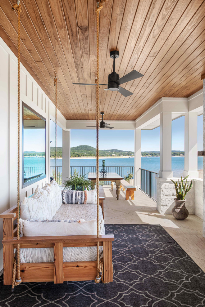 Large beach style stamped concrete metal railing back porch idea in Austin with a fireplace and a roof extension
