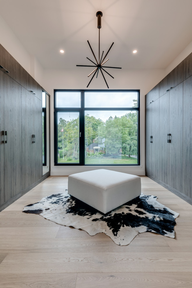 Contemporary gender-neutral walk-in wardrobe in Toronto with flat-panel cabinets, medium wood cabinets, light hardwood floors and beige floor.