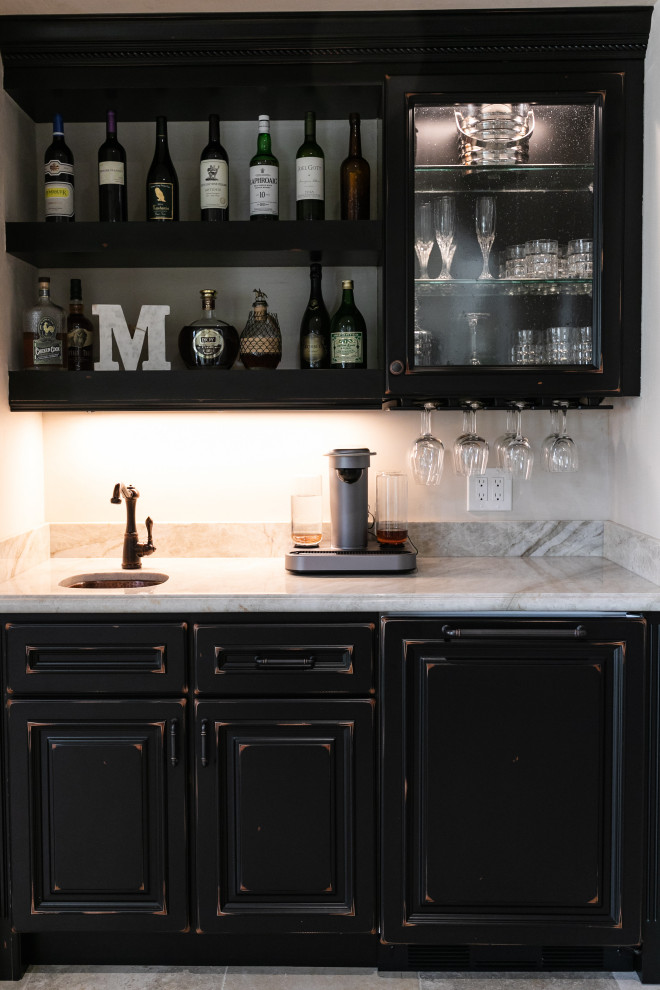 This is an example of a large mediterranean l-shaped wet bar in San Francisco with an undermount sink, raised-panel cabinets, black cabinets, quartzite benchtops, beige splashback, stone tile splashback, limestone floors, beige floor and beige benchtop.