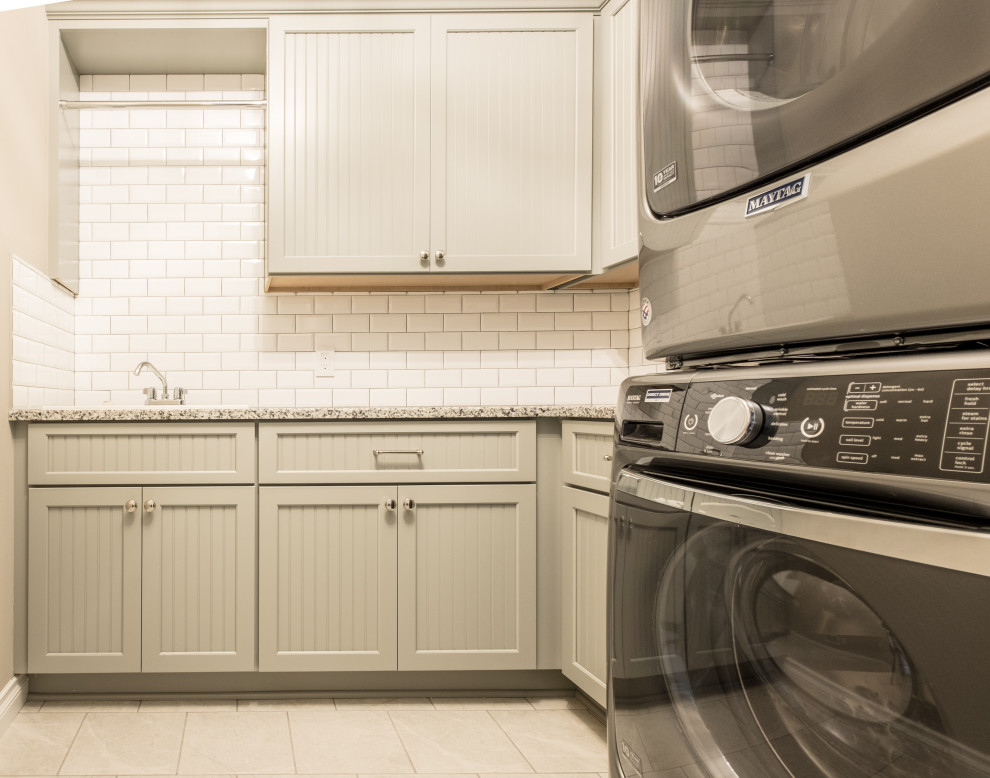 This is an example of a mid-sized country l-shaped dedicated laundry room in Detroit with a drop-in sink, granite benchtops, white splashback, subway tile splashback, beige walls, a stacked washer and dryer and beige benchtop.