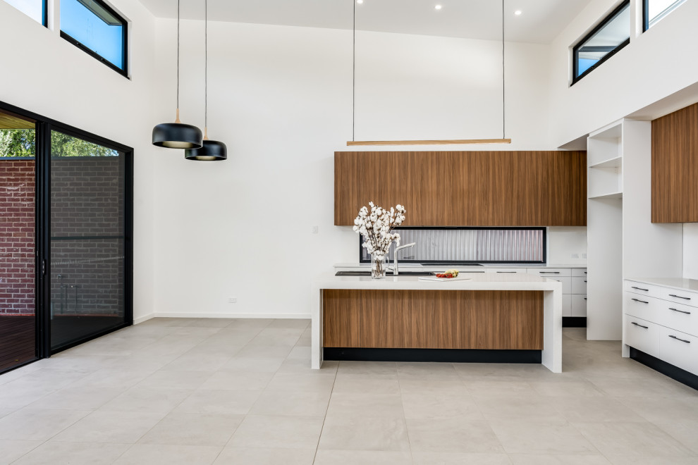 Example of a mid-sized trendy galley ceramic tile, gray floor and vaulted ceiling open concept kitchen design in Adelaide with a double-bowl sink, flat-panel cabinets, medium tone wood cabinets, quartz countertops, white backsplash, quartz backsplash, black appliances, an island and white countertops