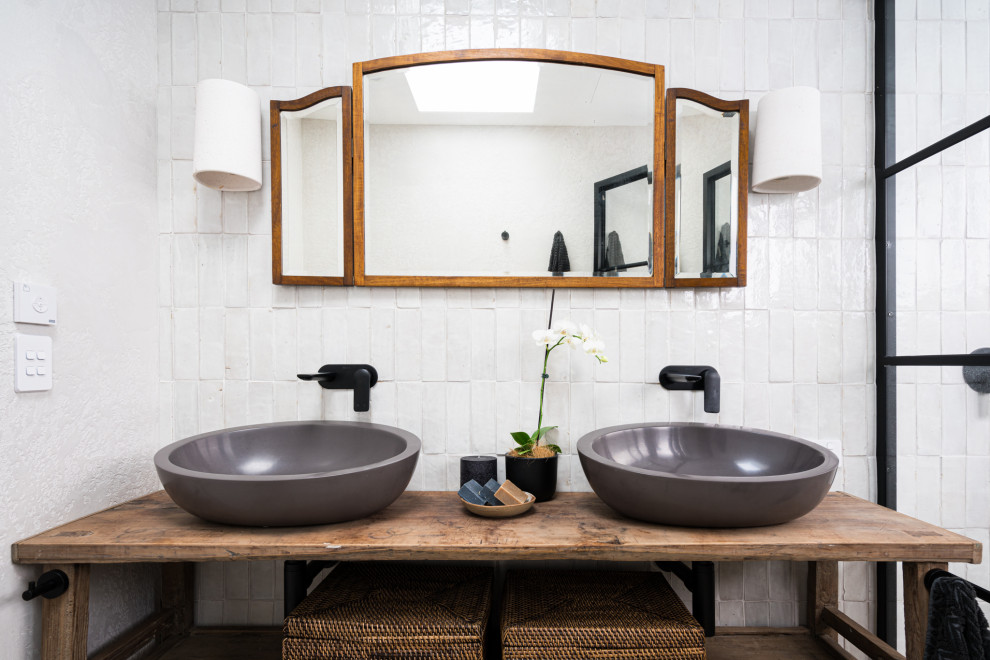 Cette image montre une salle de bain principale marine en bois brun avec un placard sans porte, un carrelage blanc, des carreaux de céramique, une vasque, un plan de toilette en bois, un plan de toilette marron, meuble double vasque et meuble-lavabo sur pied.