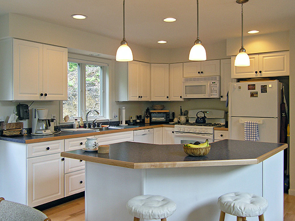 Enclosed kitchen - small transitional l-shaped light wood floor enclosed kitchen idea in Burlington with a drop-in sink, raised-panel cabinets, white cabinets, concrete countertops, stainless steel appliances and an island