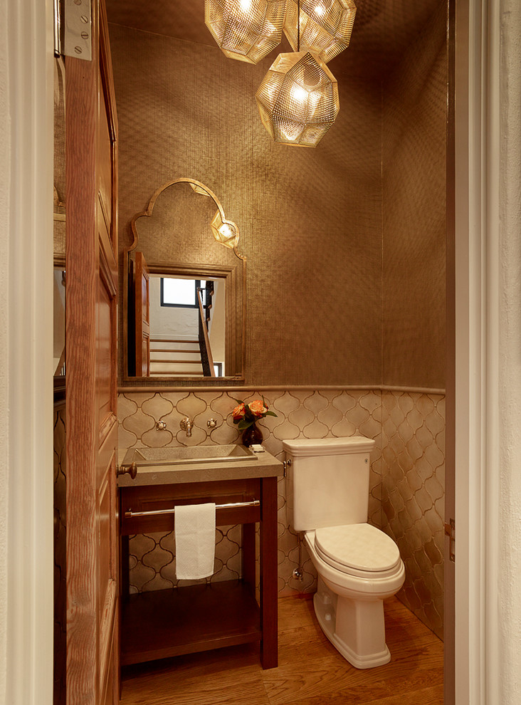 Small mediterranean powder room in San Francisco with dark wood cabinets, a two-piece toilet, beige tile, ceramic tile, medium hardwood floors, limestone benchtops, furniture-like cabinets, brown walls, a console sink and brown floor.