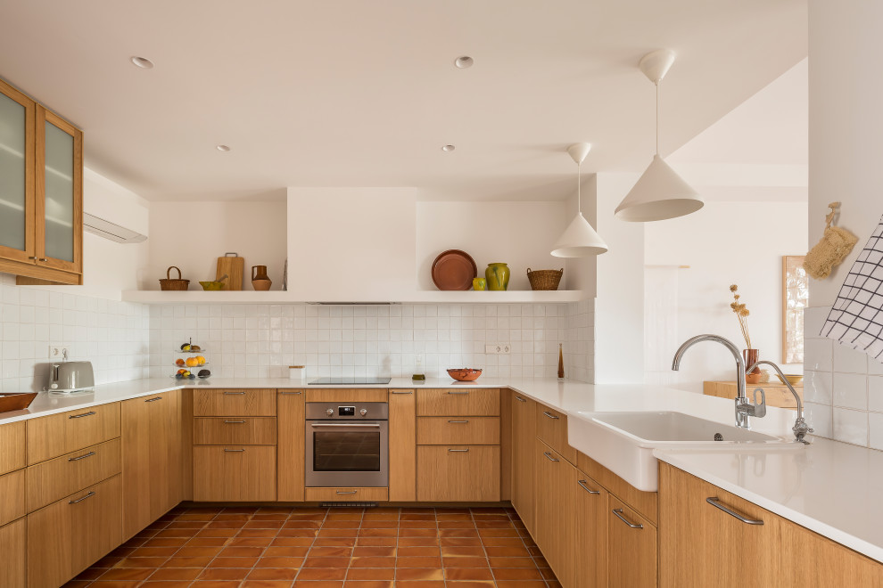 Small mediterranean u-shaped kitchen/diner in Valencia with terracotta flooring, brown floors, a built-in sink, flat-panel cabinets, brown cabinets, engineered stone countertops, white splashback, terracotta splashback, stainless steel appliances and beige worktops.