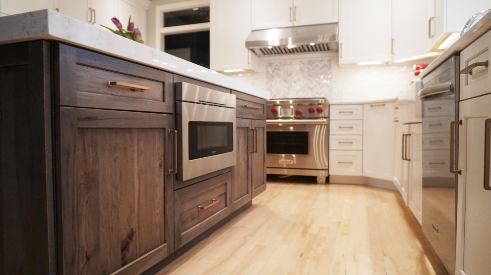 Inspiration for a transitional light wood floor open concept kitchen remodel with a farmhouse sink, recessed-panel cabinets, white cabinets, white backsplash, subway tile backsplash, stainless steel appliances, an island and white countertops