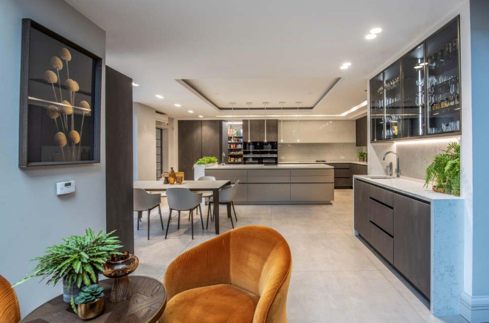 Large contemporary l-shaped eat-in kitchen in Manchester with an undermount sink, flat-panel cabinets, grey cabinets, quartzite benchtops, white splashback, granite splashback, black appliances, porcelain floors, with island, grey floor, white benchtop and coffered.