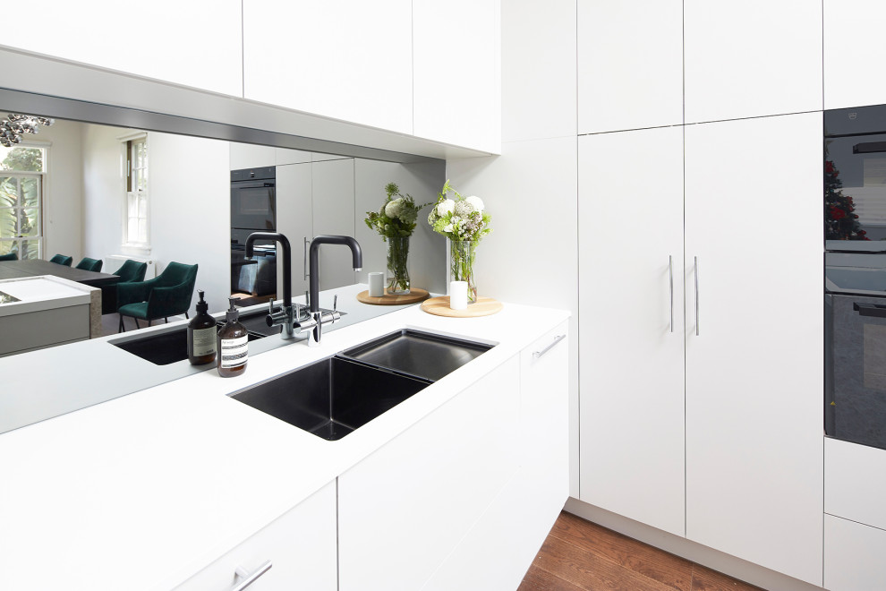 Design ideas for a small modern l-shaped eat-in kitchen in Melbourne with a double-bowl sink, grey cabinets, metallic splashback, mirror splashback, black appliances, with island, white benchtop, quartz benchtops and brown floor.