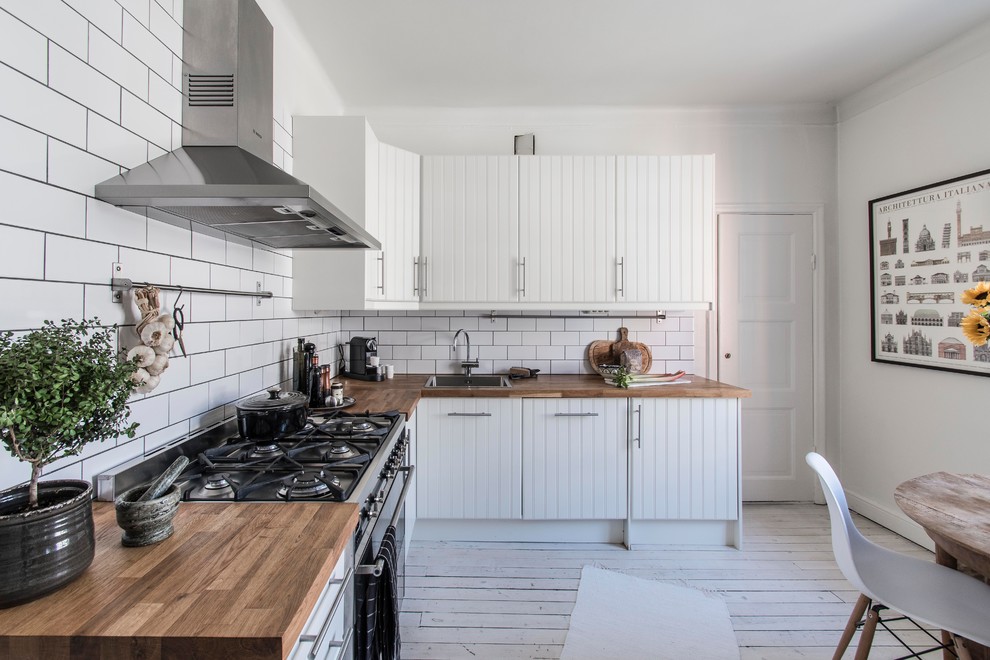 Foto på ett lantligt kök, med en nedsänkt diskho, vita skåp, träbänkskiva, vitt stänkskydd, stänkskydd i tunnelbanekakel, rostfria vitvaror, ljust trägolv och vitt golv