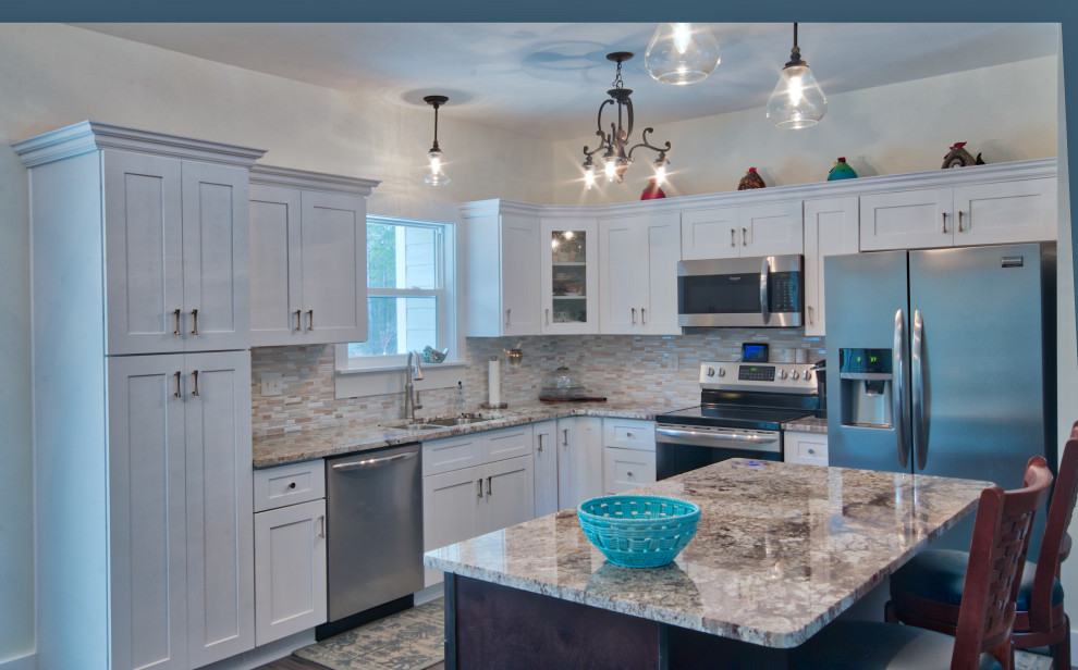 Example of a mid-sized l-shaped eat-in kitchen design with an undermount sink, shaker cabinets, yellow cabinets, granite countertops, glass tile backsplash, stainless steel appliances, an island and white countertops