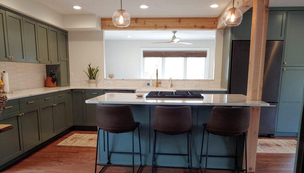 Example of a mid-sized transitional l-shaped dark wood floor eat-in kitchen design with a farmhouse sink, recessed-panel cabinets, green cabinets, quartz countertops, white backsplash, black appliances, an island and white countertops