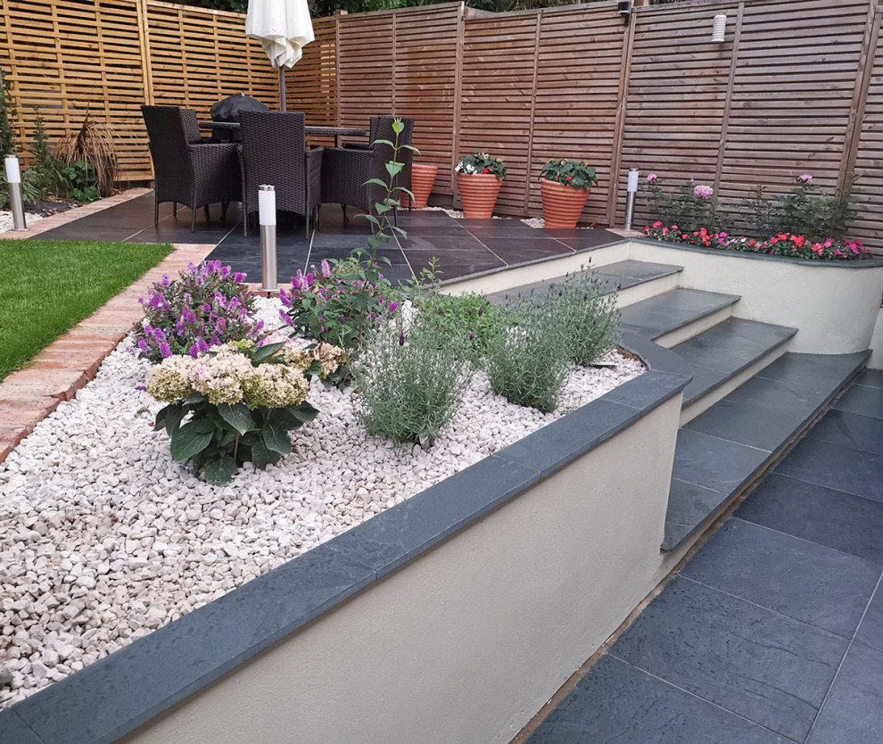 Design ideas for a mid-sized contemporary backyard patio in Hertfordshire with natural stone pavers.