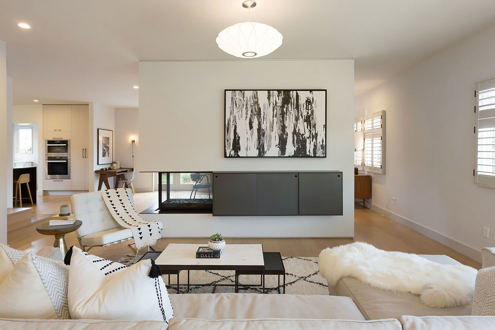 This is an example of a large midcentury formal open concept living room in San Francisco with white walls, light hardwood floors, a two-sided fireplace, a built-in media wall and a metal fireplace surround.