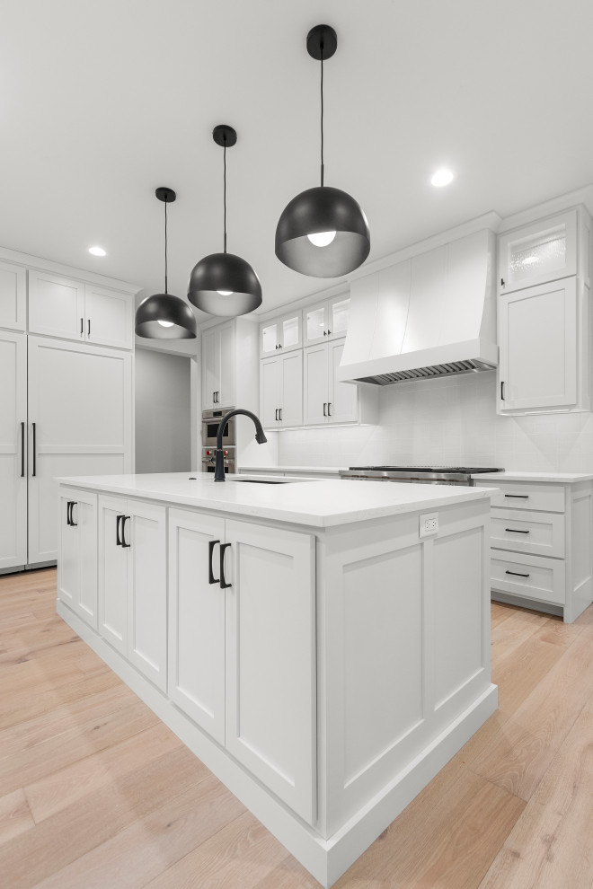 Inspiration for a large transitional u-shaped light wood floor and brown floor eat-in kitchen remodel with an undermount sink, shaker cabinets, white cabinets, quartz countertops, white backsplash, porcelain backsplash, stainless steel appliances, two islands and white countertops