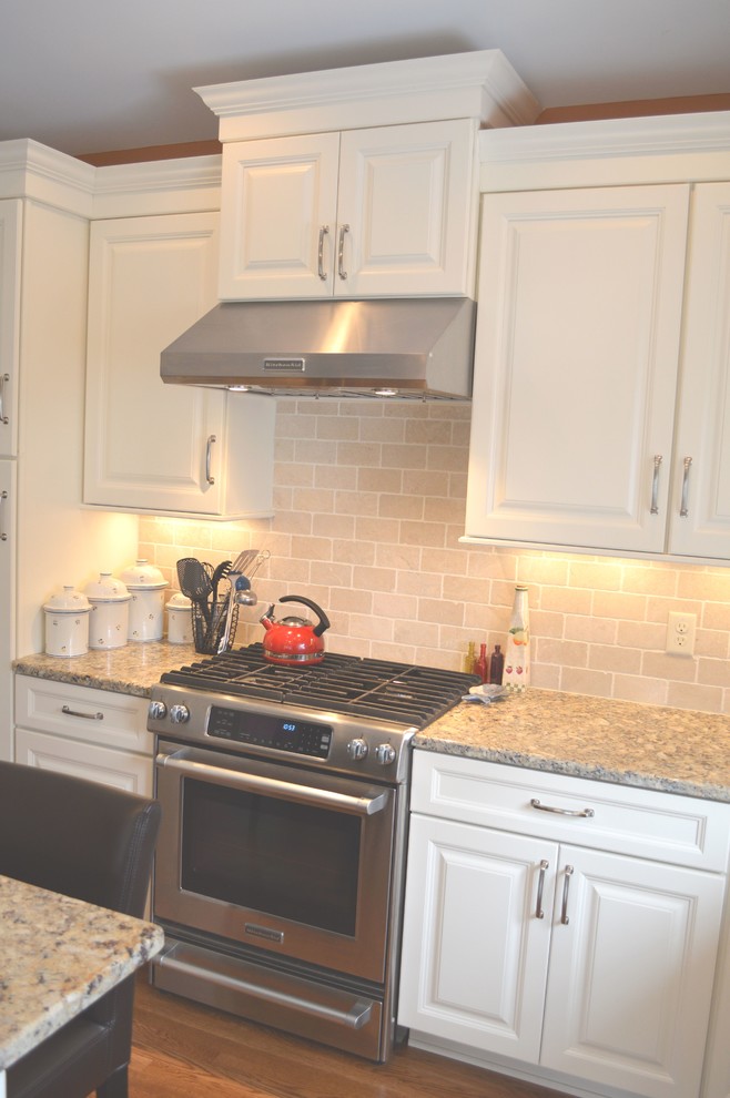 Inspiration for a large transitional l-shaped medium tone wood floor enclosed kitchen remodel in Columbus with an undermount sink, raised-panel cabinets, white cabinets, granite countertops, beige backsplash, stone tile backsplash, stainless steel appliances and an island