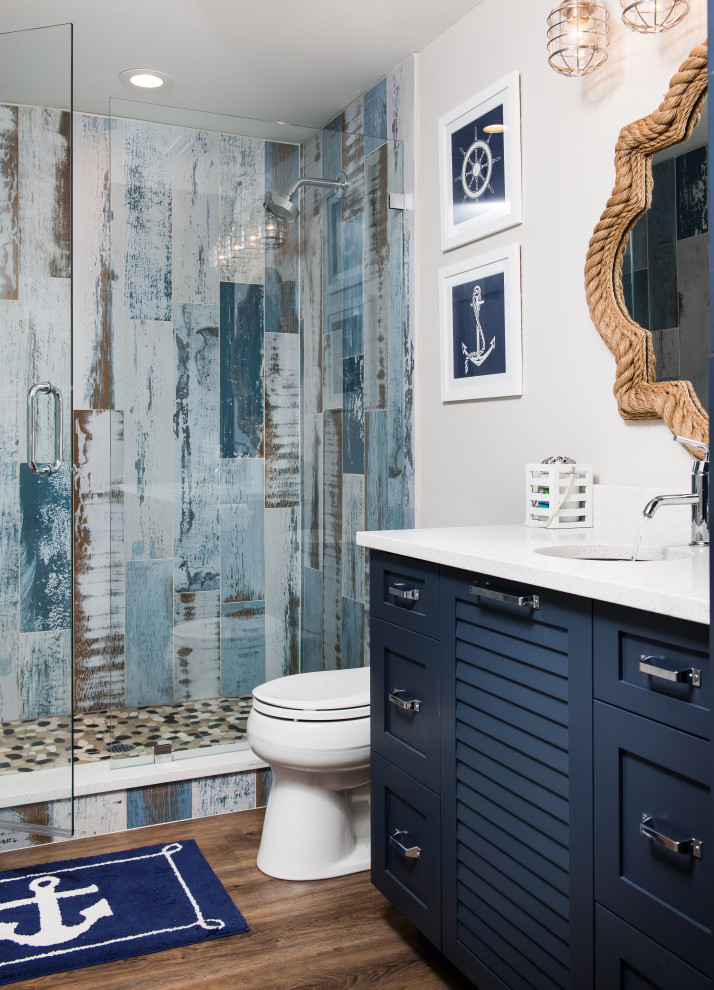 Mid-sized beach style 3/4 bathroom in Orlando with shaker cabinets, blue cabinets, an alcove shower, a two-piece toilet, blue tile, white walls, medium hardwood floors, an undermount sink, brown floor, a hinged shower door and white benchtops.