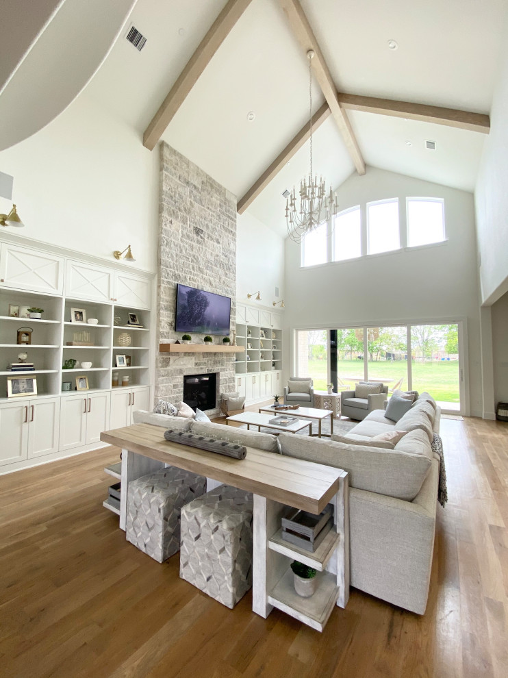 Design ideas for an expansive transitional open concept family room in Dallas with white walls, light hardwood floors, a standard fireplace, a stone fireplace surround, a wall-mounted tv, brown floor and vaulted.