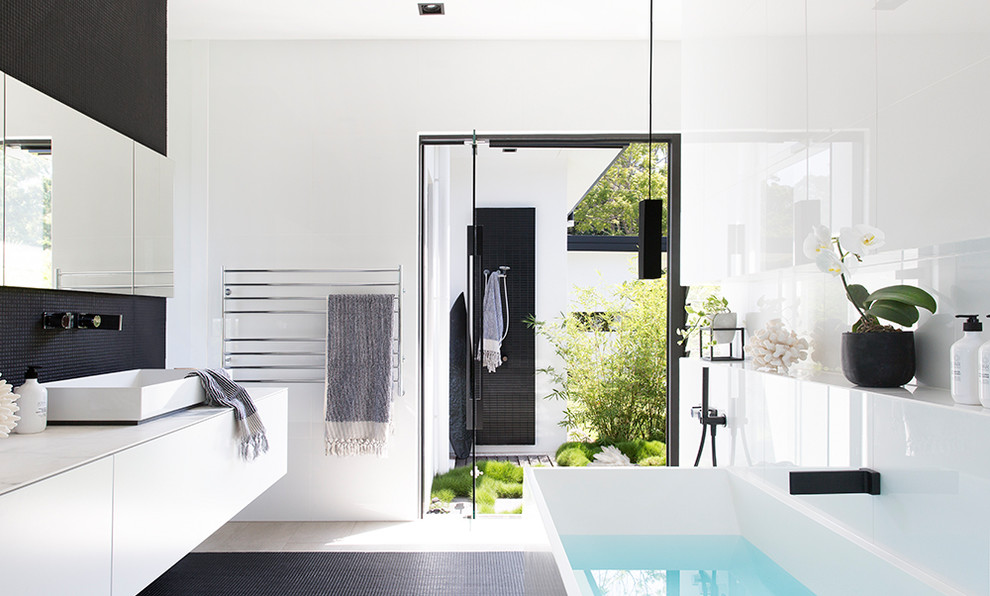 Inspiration for a modern master bathroom in Sunshine Coast with flat-panel cabinets, white cabinets, a freestanding tub, an open shower, black tile, white tile, glass tile, white walls, a vessel sink, black floor, an open shower and white benchtops.