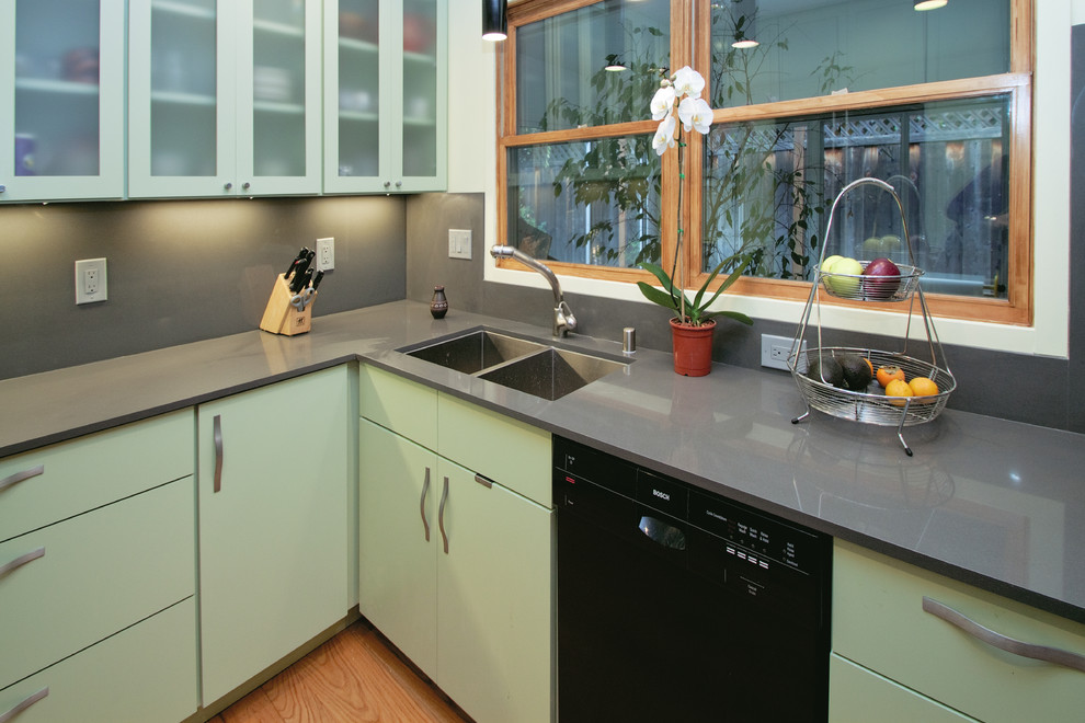 Photo of a contemporary kitchen in San Francisco with a double-bowl sink, flat-panel cabinets, solid surface benchtops, black appliances, green cabinets and grey splashback.