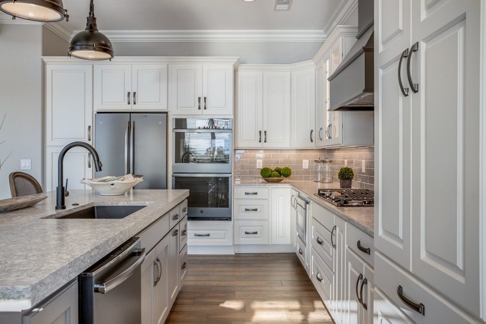 Large transitional l-shaped open concept kitchen photo with an undermount sink, raised-panel cabinets, white cabinets, quartz countertops, gray backsplash, subway tile backsplash, stainless steel appliances, an island and white countertops