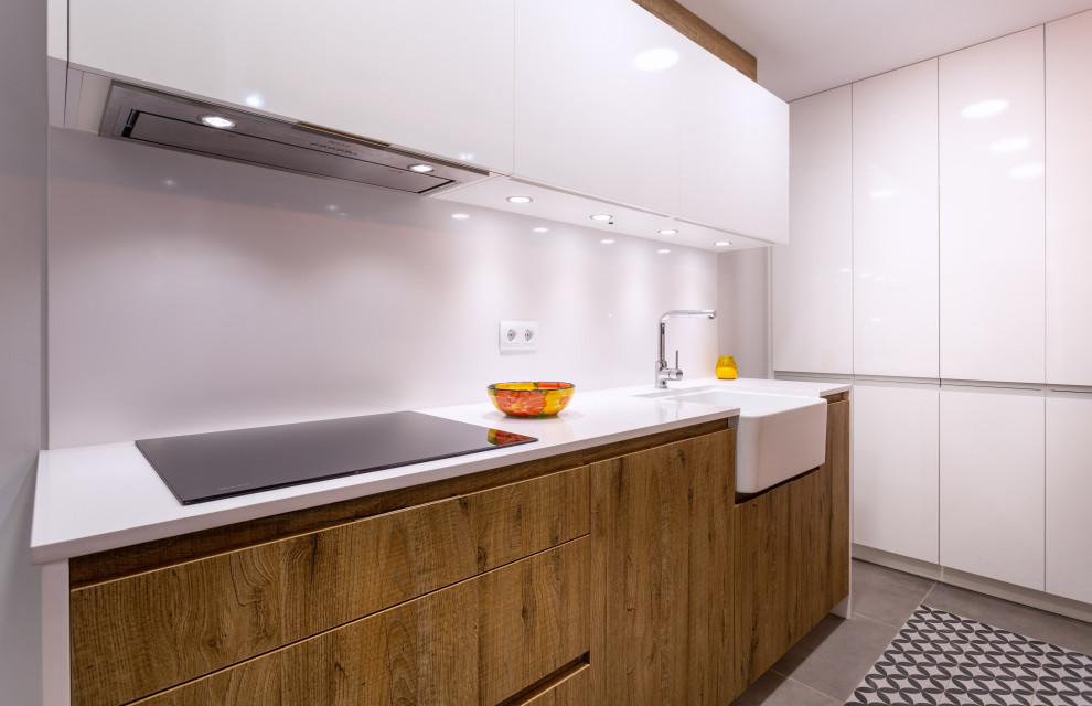 This is an example of a contemporary galley separate kitchen in Barcelona with a single-bowl sink, medium wood cabinets, white splashback, stainless steel appliances, no island, white benchtop and recessed.