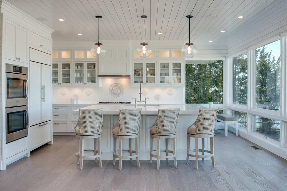 Beach style l-shaped kitchen in New York with an undermount sink, shaker cabinets, panelled appliances, light hardwood floors, with island and beige floor.