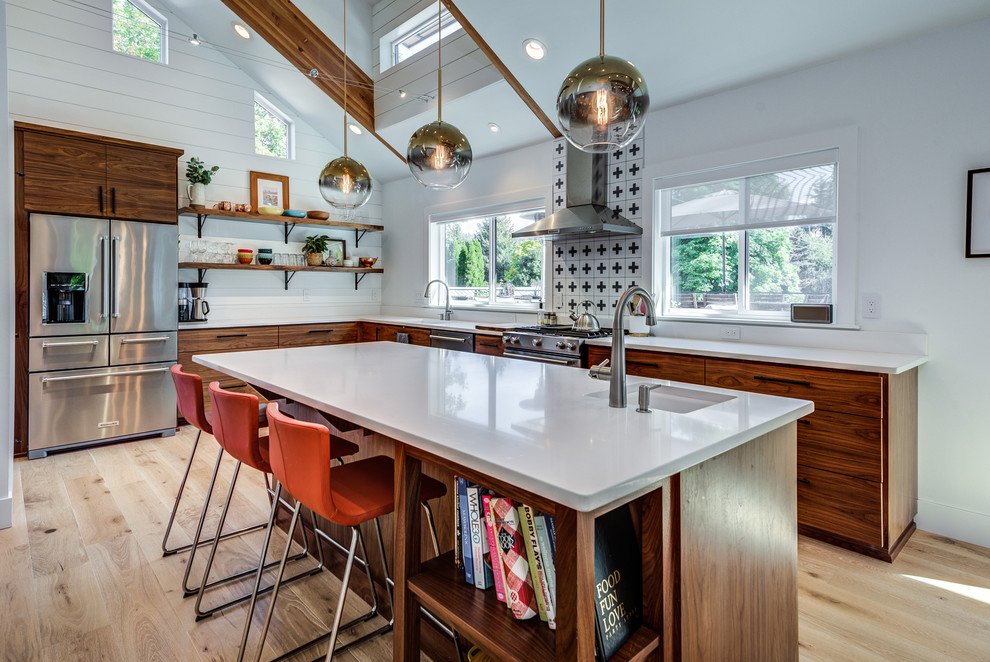 This is an example of a midcentury l-shaped kitchen in Seattle with an undermount sink, flat-panel cabinets, dark wood cabinets, multi-coloured splashback, stainless steel appliances, light hardwood floors, with island and white benchtop.