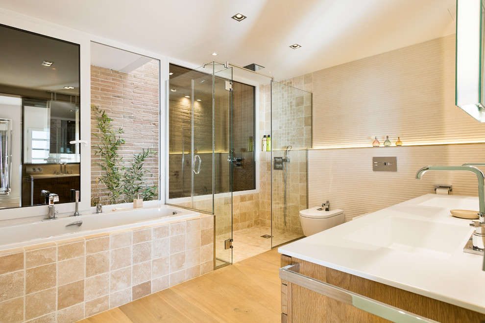 Photo of an expansive contemporary master bathroom in Barcelona with a curbless shower, beige tile, light hardwood floors, an integrated sink, a hinged shower door, a wall-mount toilet, a hot tub, ceramic tile, beige walls, onyx benchtops and beige floor.
