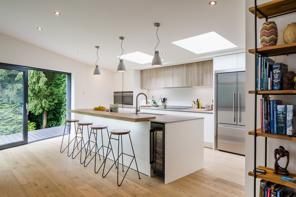 Photo of a mid-sized modern galley kitchen in Hertfordshire with flat-panel cabinets, stainless steel appliances, light hardwood floors, with island, beige floor, grey benchtop, an undermount sink and white cabinets.