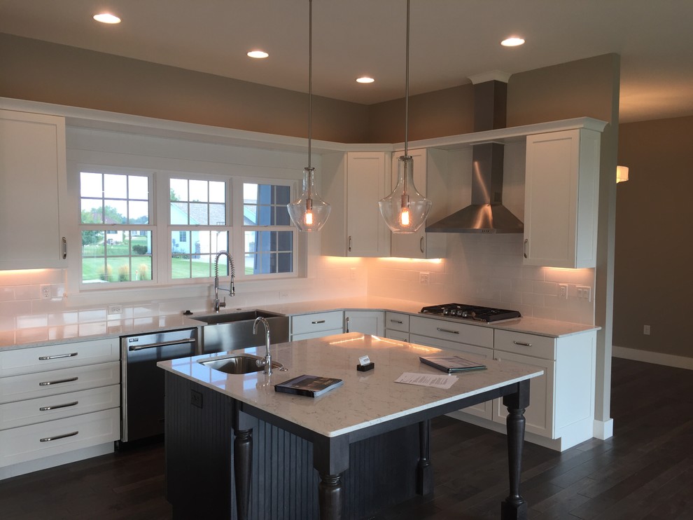 Inspiration for a mid-sized transitional l-shaped dark wood floor and brown floor kitchen remodel with a farmhouse sink, shaker cabinets, white cabinets, quartz countertops, white backsplash, ceramic backsplash, stainless steel appliances, an island and white countertops