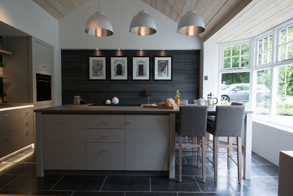 This is an example of a mid-sized country eat-in kitchen in Munich with flat-panel cabinets, grey cabinets, black appliances and with island.