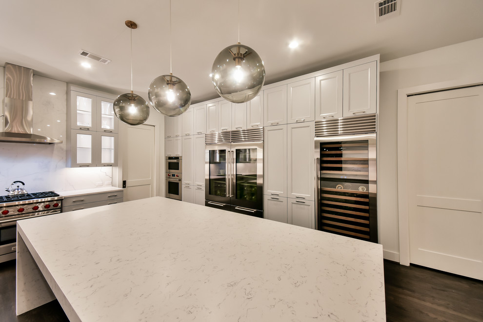 This is an example of a large contemporary u-shaped open plan kitchen in Houston with a farmhouse sink, recessed-panel cabinets, white cabinets, quartzite benchtops, white splashback, marble splashback, stainless steel appliances, dark hardwood floors, with island, brown floor and white benchtop.