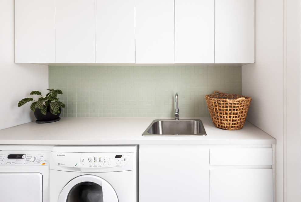 This is an example of a contemporary single-wall dedicated laundry room in Melbourne with a drop-in sink, flat-panel cabinets, white cabinets, white walls, a side-by-side washer and dryer and white benchtop.