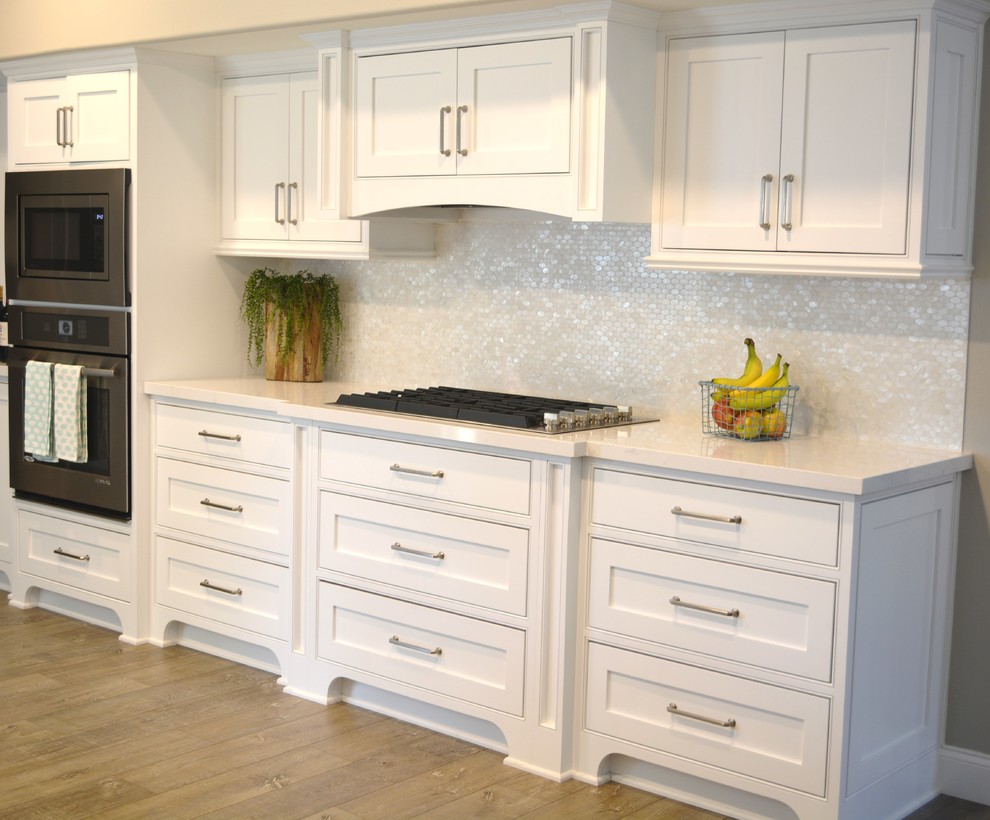 Photo of an eat-in kitchen in Orange County with an undermount sink, recessed-panel cabinets, white cabinets, marble benchtops, beige splashback, mirror splashback and with island.