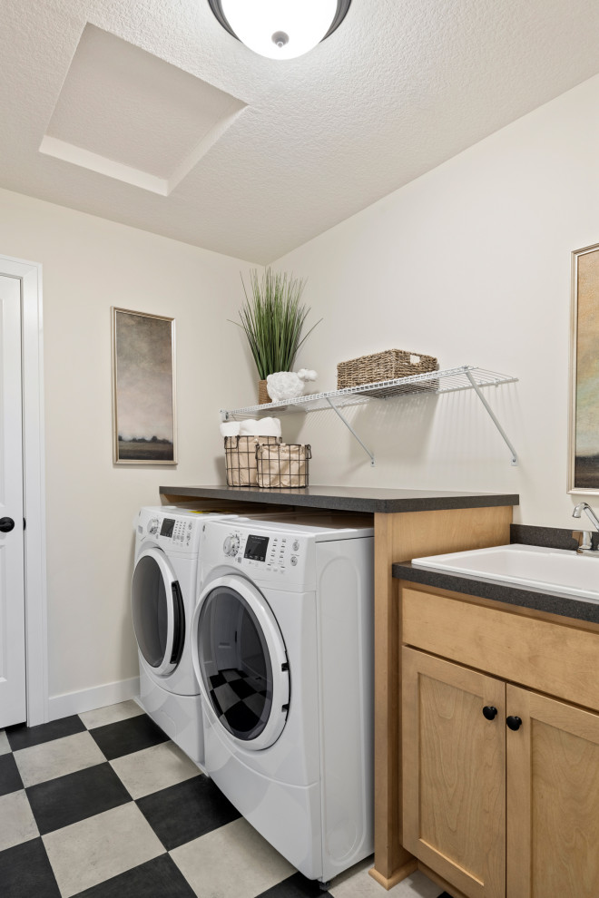 This is an example of a mid-sized country single-wall dedicated laundry room in Minneapolis with a drop-in sink, shaker cabinets, light wood cabinets, white walls, a side-by-side washer and dryer, black benchtop and multi-coloured floor.