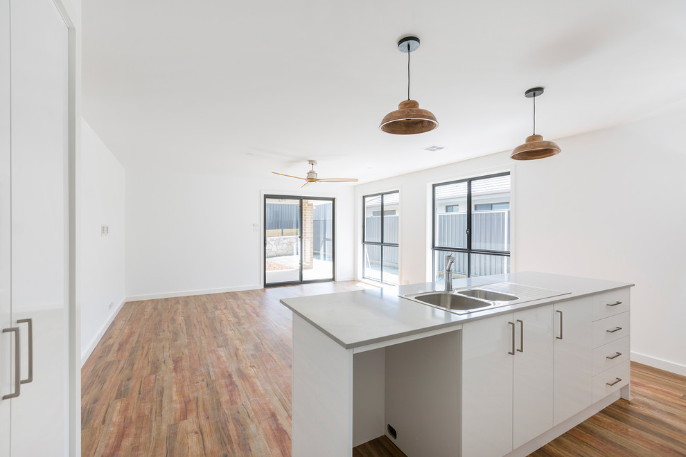 Inspiration for a small traditional galley kitchen pantry in Canberra - Queanbeyan with a double-bowl sink, flat-panel cabinets, white cabinets, quartz benchtops, grey splashback, porcelain splashback, stainless steel appliances, vinyl floors, with island, brown floor and grey benchtop.