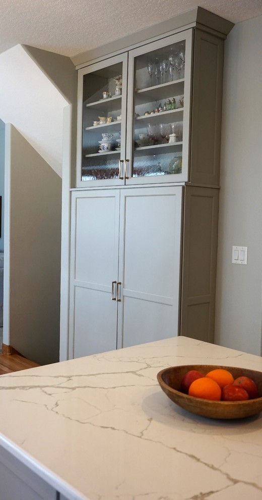 Transitional l-shaped medium tone wood floor eat-in kitchen photo with an undermount sink, recessed-panel cabinets, gray cabinets, quartz countertops, white backsplash, ceramic backsplash, stainless steel appliances, an island and white countertops
