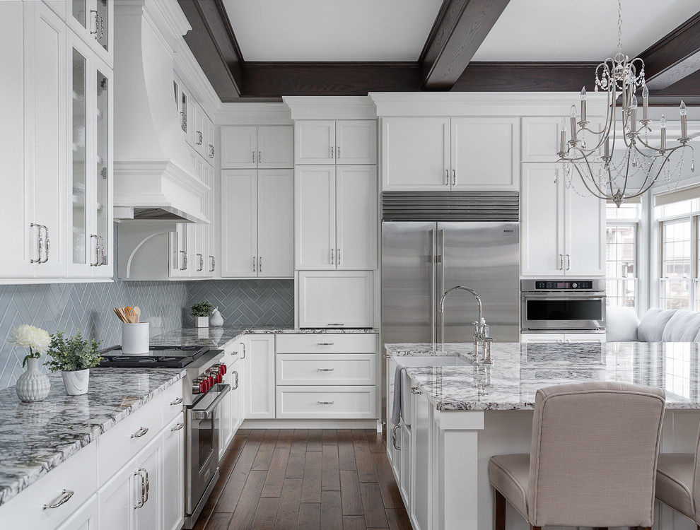 Photo of a large transitional l-shaped eat-in kitchen in Chicago with a farmhouse sink, white cabinets, granite benchtops, porcelain splashback, stainless steel appliances, dark hardwood floors, with island, brown floor and multi-coloured benchtop.