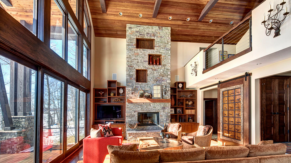 Large arts and crafts loft-style living room in New York with white walls, medium hardwood floors, a standard fireplace, a stone fireplace surround and a built-in media wall.