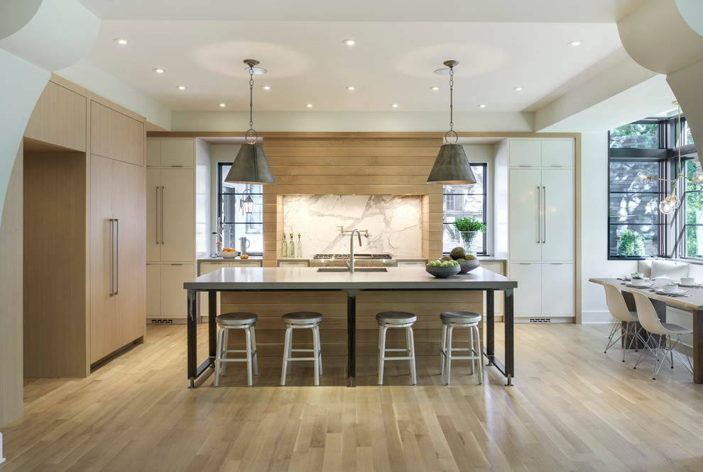 Inspiration for a large transitional l-shaped light wood floor open concept kitchen remodel in Minneapolis with an undermount sink, flat-panel cabinets, white cabinets, solid surface countertops, white backsplash, stone slab backsplash, paneled appliances and an island