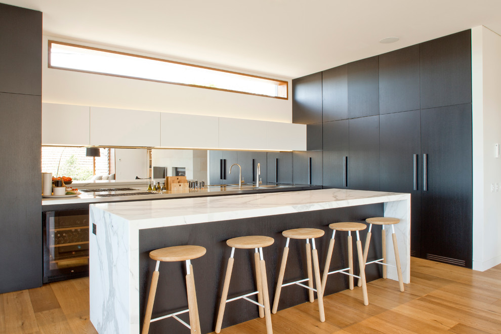 Design ideas for a contemporary galley open plan kitchen in Sydney with flat-panel cabinets, dark wood cabinets, marble benchtops, medium hardwood floors and with island.