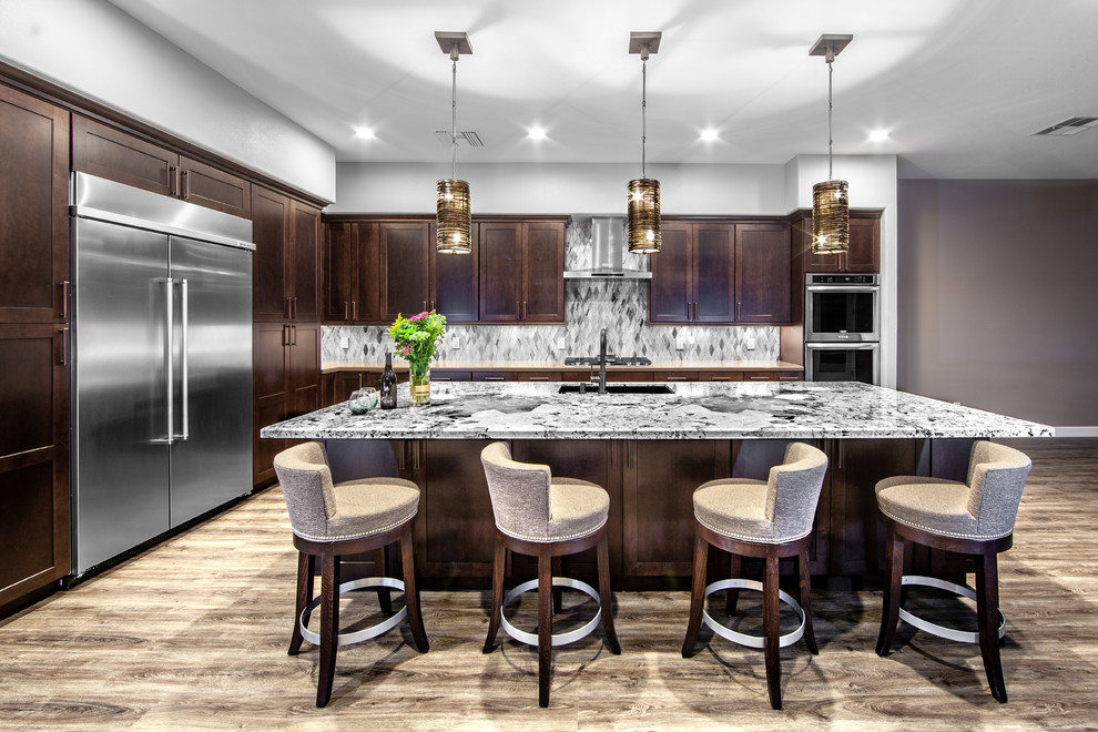 Inspiration for a large transitional l-shaped kitchen in Las Vegas with an undermount sink, shaker cabinets, dark wood cabinets, grey splashback, stainless steel appliances, medium hardwood floors, with island, brown floor and grey benchtop.