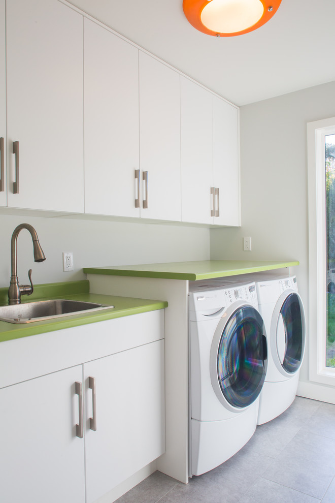 This is an example of a midcentury laundry room in Vancouver with a drop-in sink, white cabinets, laminate benchtops, white walls, concrete floors, a side-by-side washer and dryer and green benchtop.